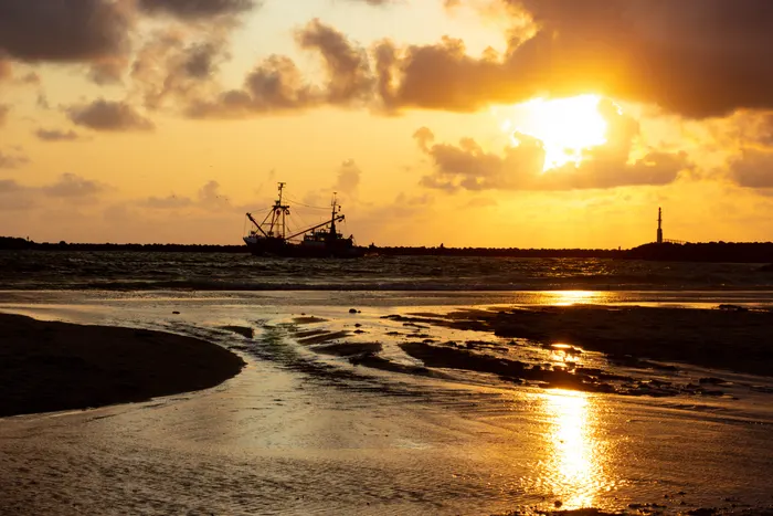 Foto eines Sonnerunterganges, während ein Fischkutter den Hafen verlässt.